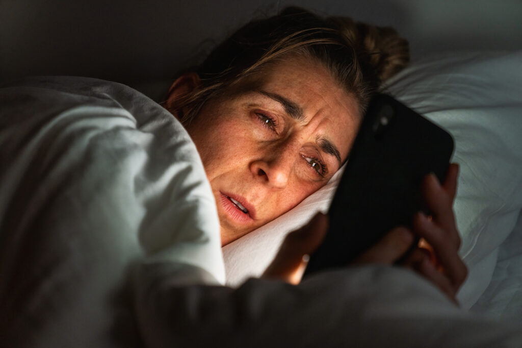 Tired Eyes (Eye Fatigue) - Causes, Symptoms & Treatment 2 Tired womans eyes being seen as she scrolls through her phone on her bed